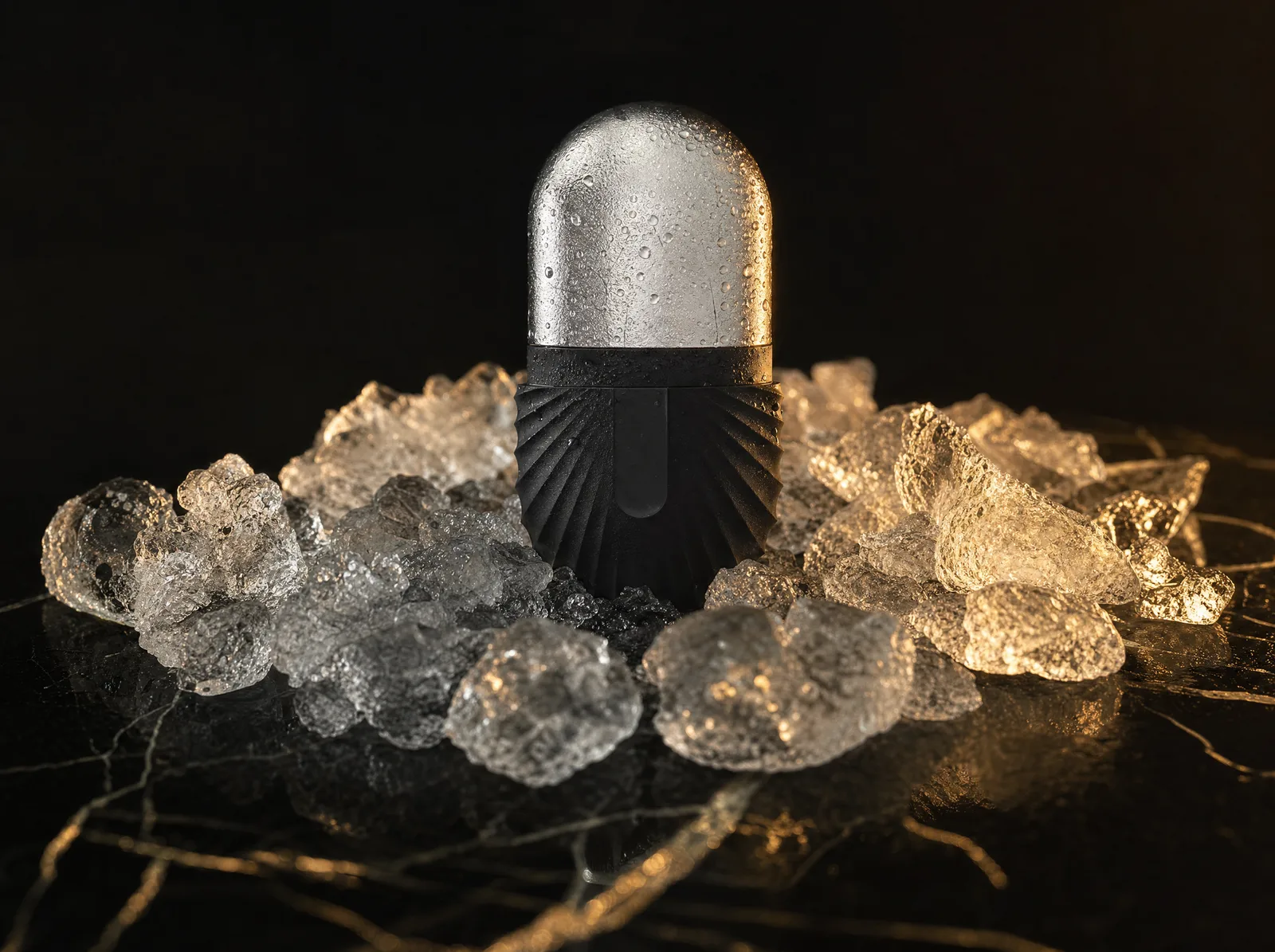 The CryoSteel Duo: a black-handled stainless ice roller emerging from crushed ice with condensation, champagne-gold rim light on black stone